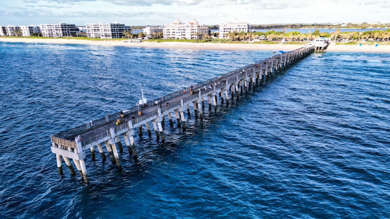Aerial view of a long concrete fishing pier over blue water on the Florida coast