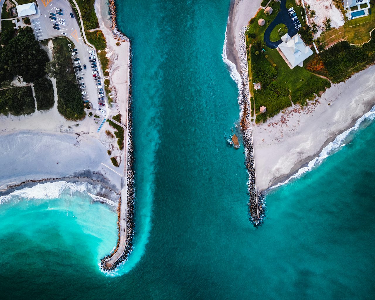 Aerial view of a Florida inlet with rock jetties on both sides, turquoise water and white sand beach