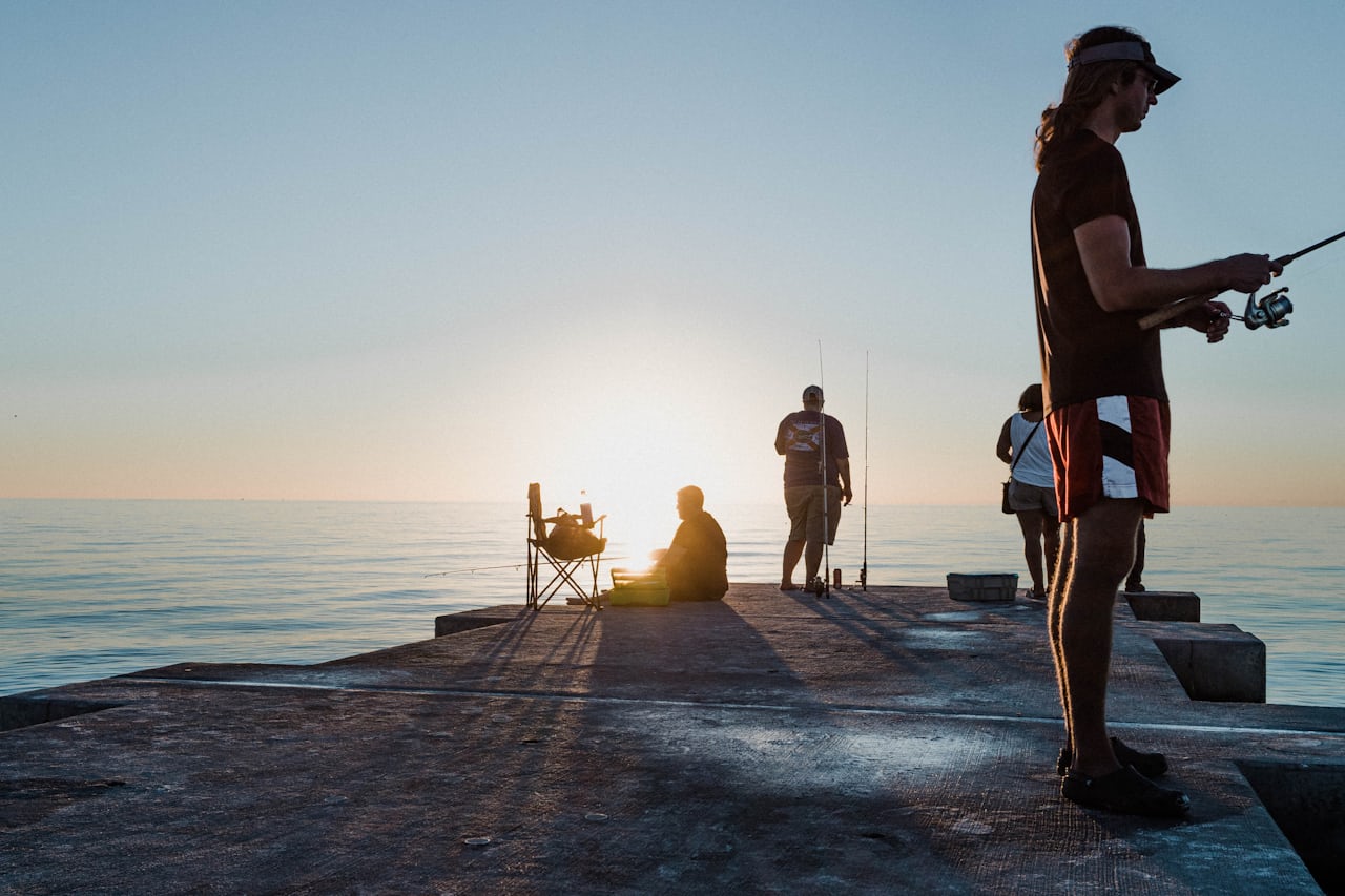 Anglers fishing from a concrete Florida pier at sunset over calm Gulf water