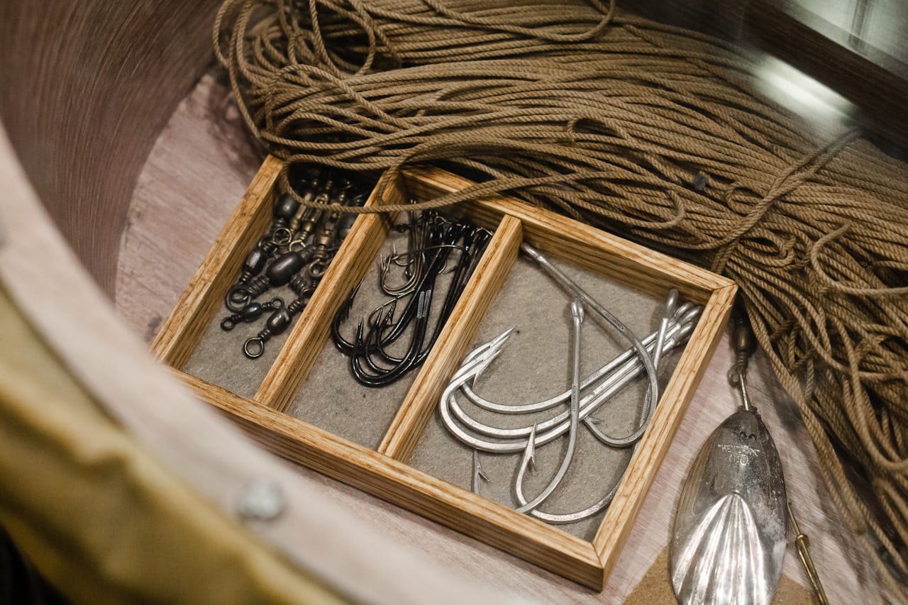 Saltwater fishing hooks, swivels and a spoon in a wooden tackle tray beside coiled line